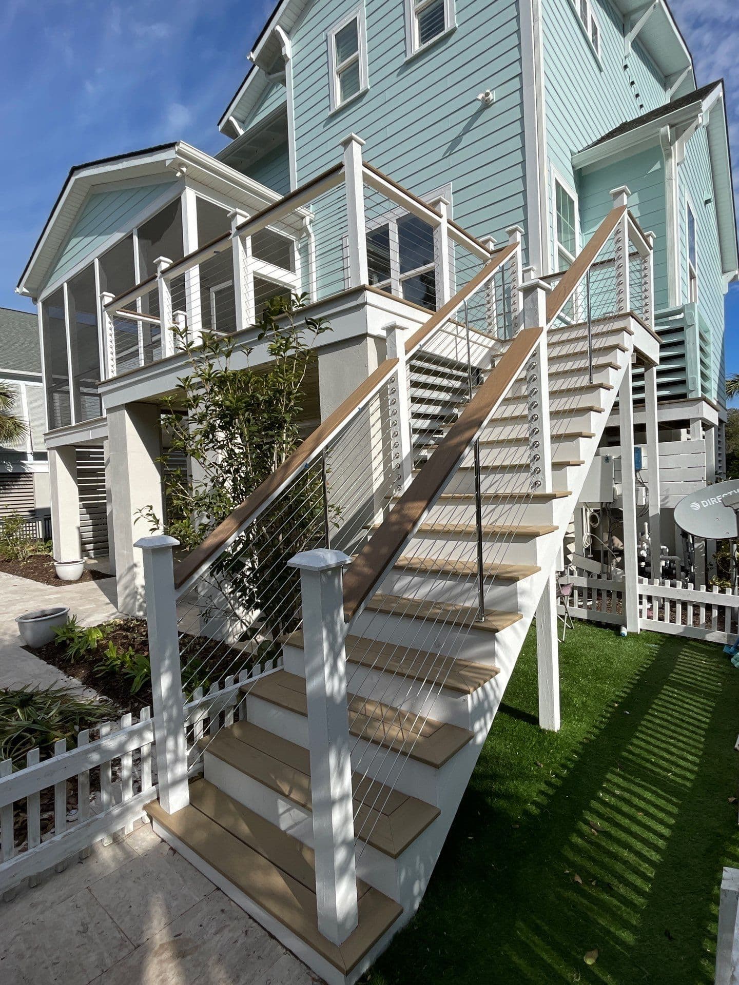 A photo of a tan and white TimberTech Decking outdoor staircase leading up to the deck of a light blue-green house in Mount Pleasant, South Carolina. The staircase has wire cables for the sides.